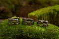 Load image into Gallery viewer, Udstillet på en seng af frodig grøn mos er tre indviklet designede mørke metalringe med naturinspirerede mønstre, hver prydet med små ædelsten. Disse ringe, kaldet Fingerring - Eryn Design - Moria (Simpel), fremviser en organisk, sammenflettet struktur, der ligner kviste eller grene. De er perfekte eksempler på håndlavede smykker.