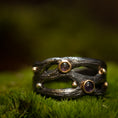 Load image into Gallery viewer, Et nærbillede af unikke håndlavede smykker hvilende på en seng af mos. Den håndlavede fingerring - Eryn Design - Moria (Med sten) har et mørkt, tekstureret bånd med organiske, grenlignende designs udsmykket med små 14 karat guldkugler og tre cabochon ædelstene, inklusive ametyst. Baggrunden er blødt sløret, hvilket understreger ringens detaljer.