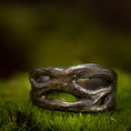 Load image into Gallery viewer, Et nærbillede af en rustik, sølvfarvet ring på en bund af grønt mos. Denne fingerring - Eryn Design - Moria (Simpel) har et organisk, sammenflettet design med uregelmæssige åbninger, hvilket giver den et naturligt og robust udseende. Baggrunden er sløret, hvilket understreger teksturen og detaljerne i dette stykke dansk design håndlavede smykker.