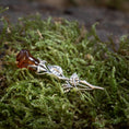 Load image into Gallery viewer, Broche Rose med Rav 925s Sølv, en sølvfarvet broche formet som en stilk med blade, holder autentisk rav, der ligner en blomsterknop, og hviler på levende grønt mos. Det detaljerede håndværk af denne romantiske gave efterligner en naturlig rose.