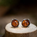 Load image into Gallery viewer, Et par Ørestikker Amber Key 925s Sølv hviler på en træoverflade. De rige, varme orange-brune sten er indkapslet i en detaljeret sølvramme med små dekorative perler, perfekt fremhævet mod den slørede baggrund.