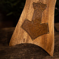 Load image into Gallery viewer, Nærbillede af bunden af et træstolsarmlæn, med et indgraveret og dekoreret design, der minder om Thors Hammer fra nordisk mytologi. Træet har en poleret finish, og messingnitter fremhæver vikingeudsmykningen smukt, ligesom det håndværk, der ses på Drikkehorn Raw med Thors Hammer Holder.