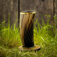 Load image into Gallery viewer, Et højt, indviklet designet Drikkeglas Horn med mønster (300 ml) med en gylden kant, placeret på en træskranke, er placeret på levende grønt græs. Baggrunden har en rustik trævæg.