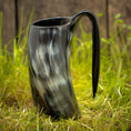 Load image into Gallery viewer, Et Vikingekrus Nature Horn (600-800ml) med et håndtag, prydet i et marmoreret sort og gråt mønster, står oprejst på græsklædt terræn med en træbaggrund. Dette stykke legemliggør essensen af vikingekrus, der forener tradition og håndværk.