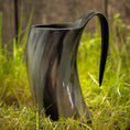 Load image into Gallery viewer, Et poleret, buet Vikingekrus Nature Horn (600-800ml) med et håndtag, stående på græsklædt jord med en sløret træbaggrund. Dette sorte drikkehorn har en blank finish og naturlige teksturerede mønstre, hvilket giver et unikt og rustikt udseende.