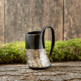 Load image into Gallery viewer, En håndlavet Mini Vikingekrus Horn Rifflet (100 ml) med en struktureret, ribbet nederste halvdel sidder på en rustik træoverflade. En plet af grønt mos er i baggrunden, hvilket skaber naturlige, jordnære omgivelser, der minder om Roskilde showroom.