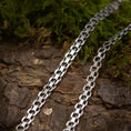 Load image into Gallery viewer, Nærbillede af to Halskæde Bismark 5,8mm 925s Sølv halskæder liggende på en struktureret træoverflade med grønt mos i baggrunden. De sammenlåsende led reflekterer lyset, fremhæver deres polerede finish og skaber et råt udtryk, der står i smuk kontrast til de naturlige elementer.
