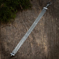 Load image into Gallery viewer, Armbånd Bismark 1,7mm 925s Sølv ligger fladt på en træoverflade. Grøn mos dekorerer det øverste venstre hjørne og tilføjer et naturligt præg til den rustikke baggrund. 925s Sterling sølv armbånd har sammenlåsende led i et Bismark fletning mønster og er sikret med en hummer lås.