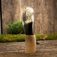 Load image into Gallery viewer, En dekorativ Drikkehorn Templar med et udskåret pentagram-symbol vises opretstående på en rustik træoverflade. Grønt løv og en trækulisse danner en naturlig ramme om det polerede bøffelhorn, der minder om vikingemarkeder.