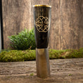 Load image into Gallery viewer, En poleret, mørkfarvet Drikkehorn Templar med guldkant og dekorativt knudedesign sidder på en træoverflade. Scenen har grønt mos og planter i baggrunden, der fremkalder vikingemarkedernes rustikke, naturlige stemning.