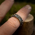 Load image into Gallery viewer, Nærbillede af en hånd, der viser en stak af tre hamrede 925 Sterling sølv ringe med små gyldne perler, fra Fingerring - Eryn Design - Eni kollektionen. De stabelbare ringe, som bæres på langfingeren, har et elegant dansk design, med en let sløret baggrund, der gør opmærksom på smykkets indviklede detaljer.
