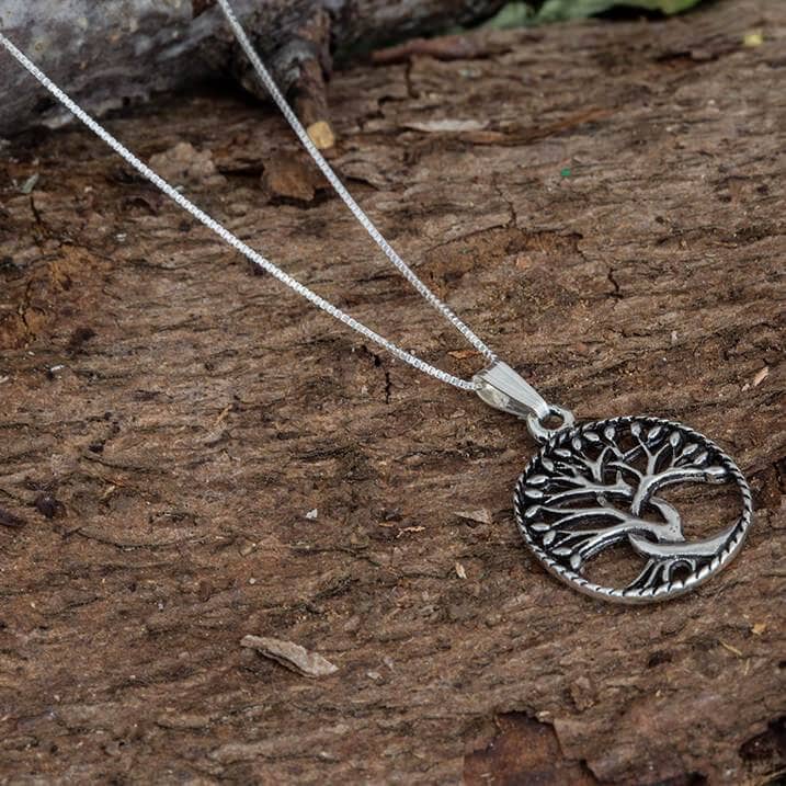 En 925s Sterling sølv vedhængshalskæde med et Tree of Life-design hviler på en tekstureret træoverflade. Vedhængets sarte grene og rødder er kunstfærdigt udformet, hvilket symboliserer vækst og forbindelse. Halskæde Venezia 925s Sølv 0,8 mm kæde er tynd, hvilket tilføjer smykkets indviklede udseende.