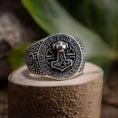 Load image into Gallery viewer, Sølvring Thors Hammer 925s Sølv-ringen viser stolt et detaljeret Mjölnir (Thors Hammer)-emblem i midten, omgivet af indviklede runer og mønstre. 925 Sterling sølv ringen hviler på en struktureret stensokkel med en sløret grøn bladagtig baggrund.
