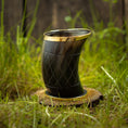 Load image into Gallery viewer, Drikkeglas Horn med Mønster (100 ml), med en guldkantet kant, står oprejst på en træbund. Hornet har et indviklet mønster på kryds og tværs og vises på en græsklædt udendørs overflade med en sløret baggrund af frodigt grønt og træhegn.
