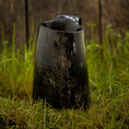 Load image into Gallery viewer, Vikingekrus Thors Hammer Horn (600-800 ml), et poleret sort hornkrus med et ætset design af Thors Hammer, vises på levende grønt græs mod en rustik træbaggrund.
