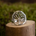 Load image into Gallery viewer, Livets Træ Yggdrasil Fingerring 925s Sterling Sølv viser et indviklet trædesign med bare grene indkapslet i en cirkulær ramme. Dette detaljerede stykke er elegant vist på et lille stykke træ mod en sløret grøn baggrund.
