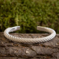 Load image into Gallery viewer, Et Armbånd Bangle Empor 925s Sterling Sølv hviler på et stykke bark, med grønt mos sløret i baggrunden. Armbåndet har et indviklet, vævet design.
