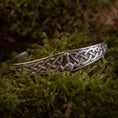 Load image into Gallery viewer, Et detaljeret Armbånd Armbånd Mjølnir lavet af 925'erne Sterling Sølv, med indviklede keltiske knudemønstre og et lille dragehoved i midten, sat mod en baggrund af frodigt grønt mos.
