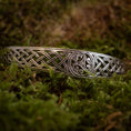 Load image into Gallery viewer, Armbånd Bangle Triskele 925s Sterling Sølv, der viser fint detaljerede keltiske knudedesigns, herunder en elegant triskele, hviler på en seng af frodig grøn mos. Armbåndets håndværk har kunstfærdige symmetriske mønstre, der fremkalder traditionelle kunstneriske stilarter.
