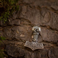 Load image into Gallery viewer, En detaljeret Thors Hammer Vedhæng 925s Sterling sølv Celtic hviler på bark med ru tekstur. Vedhænget er lavet af massivt 925s sølv og har indviklede nordiske designs og keltiske mønstre, omgivet af pletter af grønt mos, hvilket skaber en naturlig og jordnær stemning.
