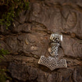 Load image into Gallery viewer, Thors Hammer Vedhæng 925s Sterling sølv Celtic, et sølvvedhæng designet til at ligne Mjolnir (Thors hammer), har indviklede nordiske og keltiske mønstre. Den fint udformede 925 sterling sølv hammer vises mod en struktureret træbark baggrund, med mos rundt om kanterne, der tilføjer et naturligt præg til billedet.
