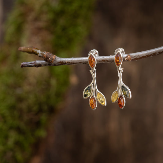 Elegant Boroi 925s drop earrings, made of 925s silver and adorned with multicolored gemstones, hang from a short tree branch. Each earring has a curved design with four small marquise stones in green, amber and yellow against a blurred earthy background.