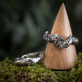 Load image into Gallery viewer, To "Fingerring - Eryn Design - Trial by Fire" stykker i 925s Sterling sølv vises på baggrund af grønt mos. Den ene ring hviler på jorden, og den anden er balanceret oprejst på et trækeglestativ. Begge håndlavede smykker har en ru, struktureret overflade og har små, indlejrede ædelstene.
