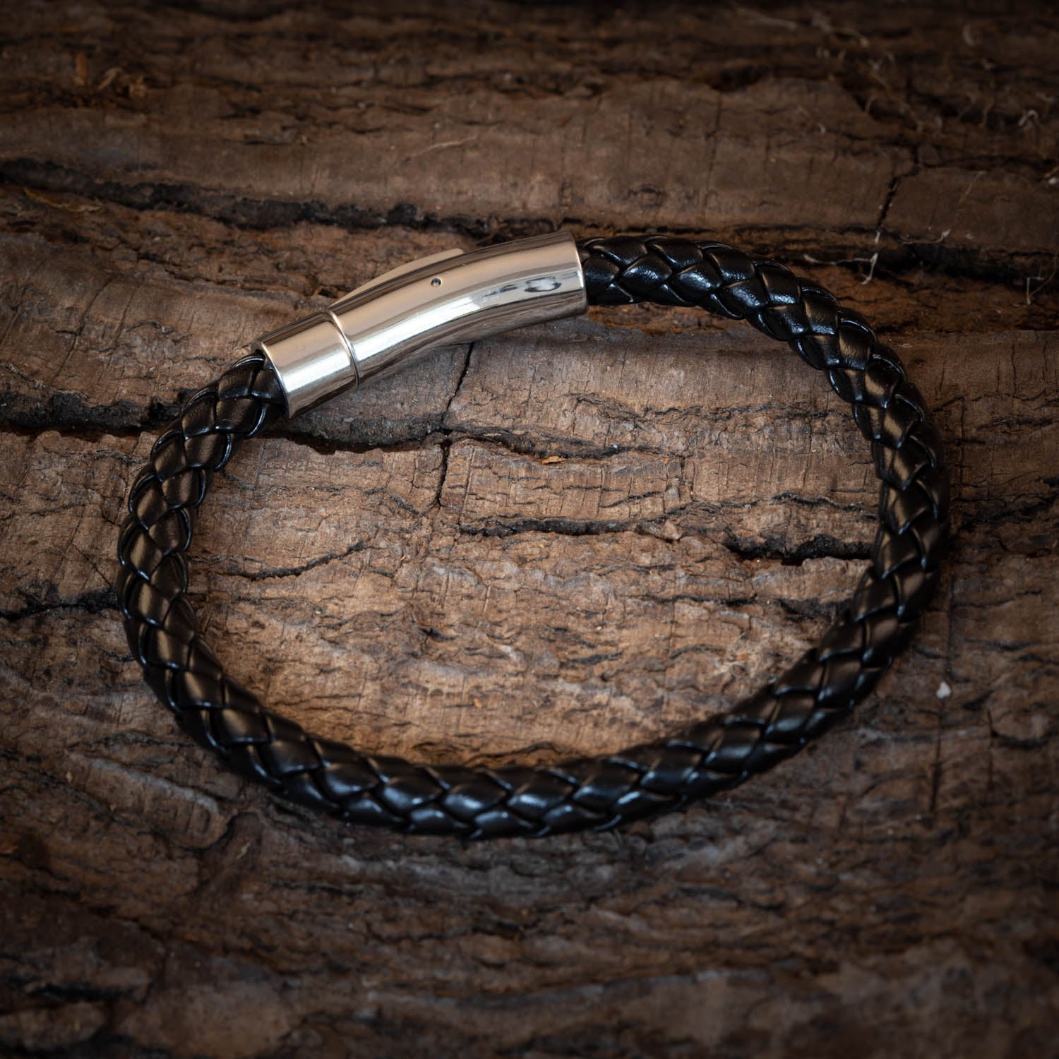 Close-up of a leather bracelet with a Steel clasp, featuring a shiny Steel buckle, placed on a rough wooden surface. The wood’s texture contrasts with the bracelet’s smooth, sleek design.
