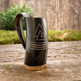 Load image into Gallery viewer, Et Vikingekrus Valknut Horn (600-800 ml) med nordiske symboler hviler på en træoverflade prydet med grønt mos og en plante i baggrunden, der fremkalder vikingearvens ånd.
