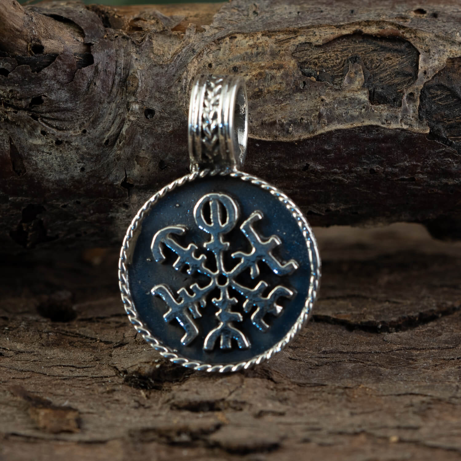 Rune Amulet Vejviser Vedhæng 925s Sterling Sølv vedhæng, med indviklede sølvdesigns og et symmetrisk Vegvísir-symbol på en mørk baggrund, hænger mod en ru træoverflade. Det runde vedhæng er prydet med en snoet reblignende kant og detaljeret metalarbejde.